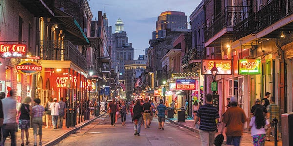 Sightseers, revelers and diners stroll down a brightly lit street in New Orleans.