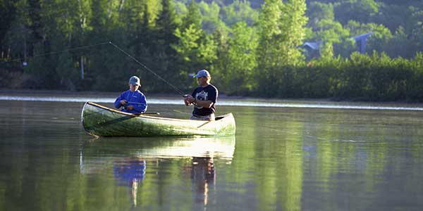 Two people in a canoe with fishing poles on a calm lake.
