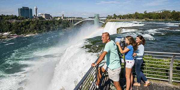 A man, girl and woman lean on a railing overlooking awesome Niagara Falls