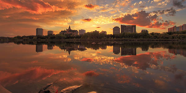 A skyline at dusk reflected perfectly by still waters. 