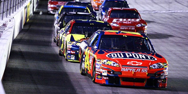 A red stock ca with the Du Pont logo leads a pack of competing cars on a track.