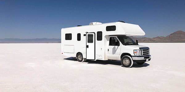 A white Class C motorhome parked on salt flats. 