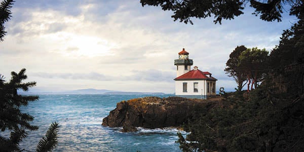 A small lighthouse and cabin perched on a rocky ocean coast.