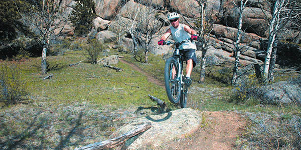 Man wearing helmet and shades mountain biking over rocky trail.
