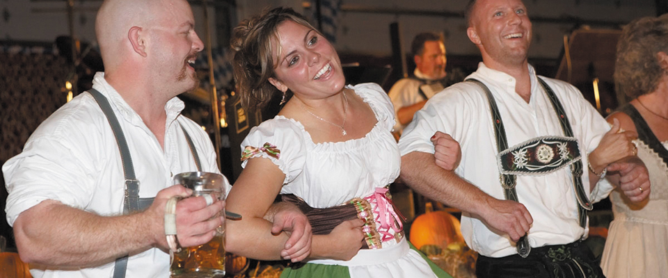 Revelers dressed in Bavarian garb join arms and sing. 