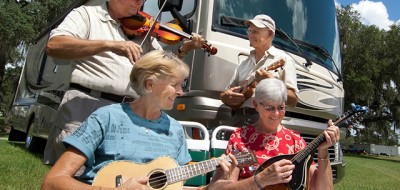 Two elderly couples playing violin, banjo and guitar next to motorhome, outside
