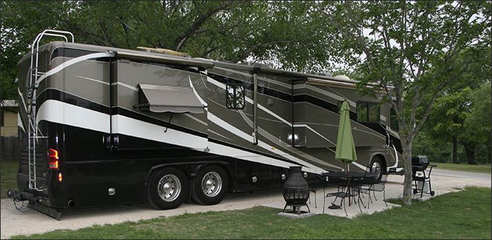 Side view of large black, grey and white motorhome with green umbrella and chairs out front