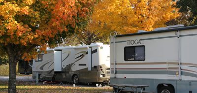 Two RVs parked in campground with fall colored trees and orange and yellow leaves on the ground
