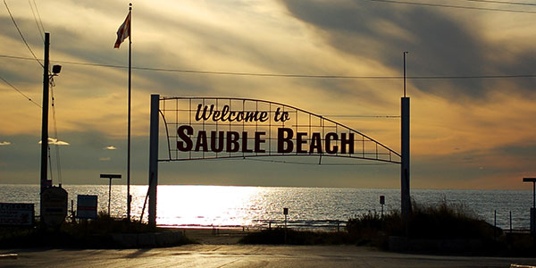A "Sauble Beach" sign at sunset against the water.