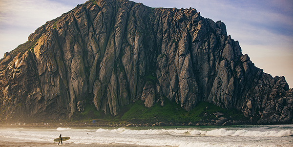 Morro Rock dwarfs a surfer on the shore.