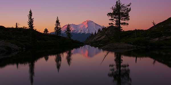 Mount Shasta reflected upon a placid lake at dusk.