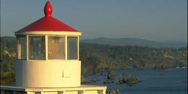 A red-roofed lighthouse overlooks an ocean coast.