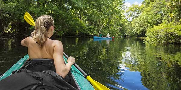 A woman kayaks through swampy river.