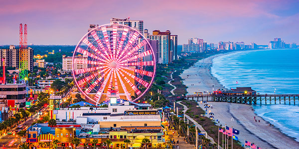 Ferris wheel covered in lights spins on a seashore. 