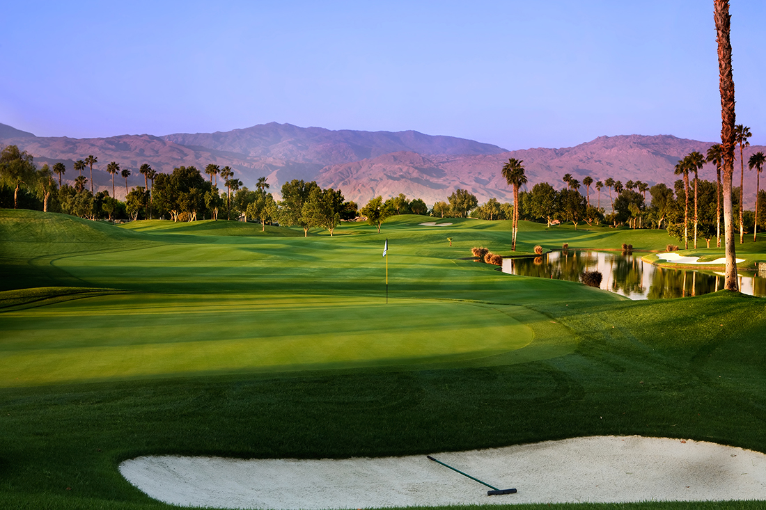 A lush golf course with rugged mountains in background.