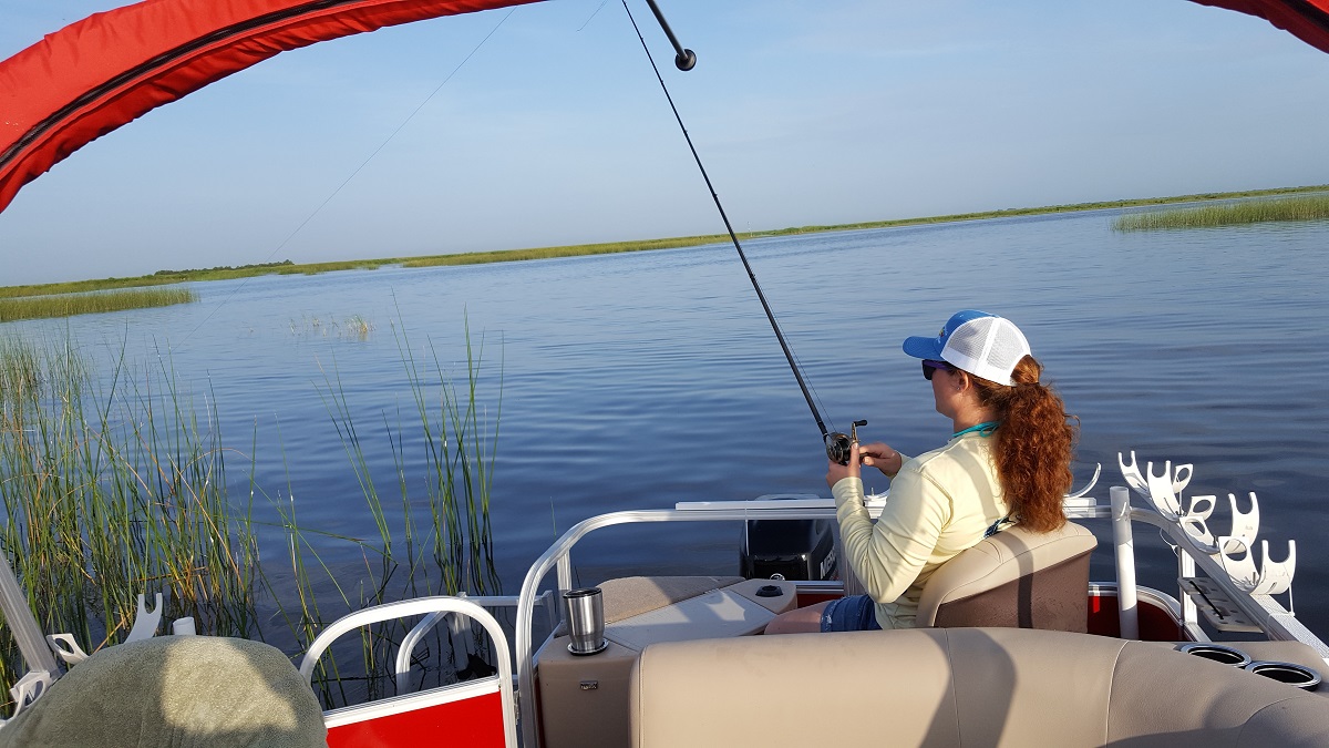Woman wearing baseball hat fishing from back of boat on sunny day