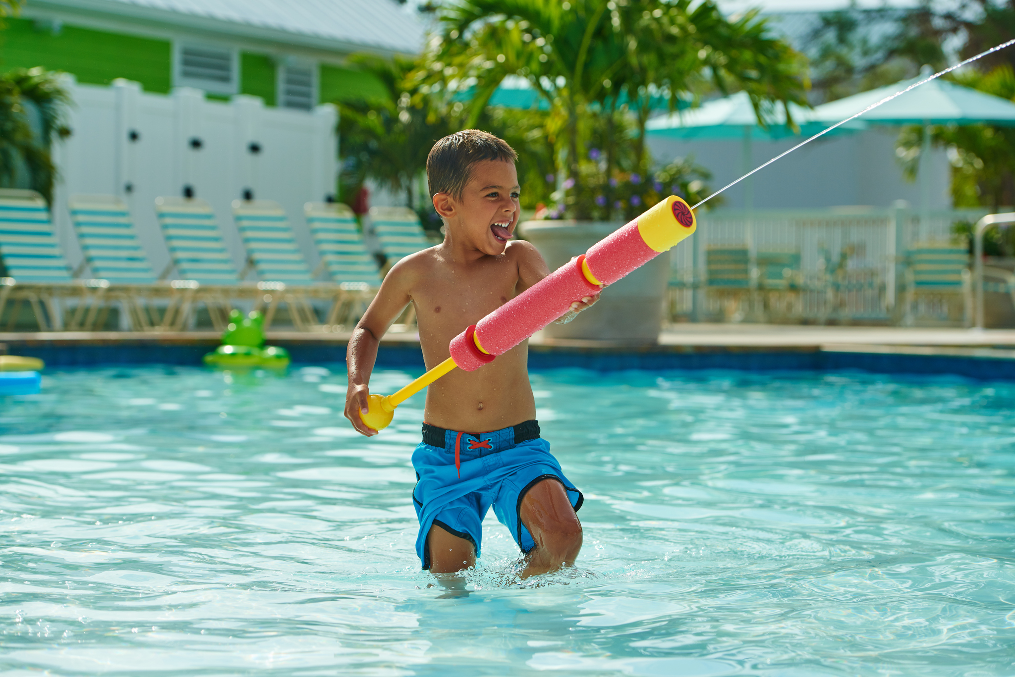 Young boy wearing blue bathing suit shooting water gun and smiling in pool
