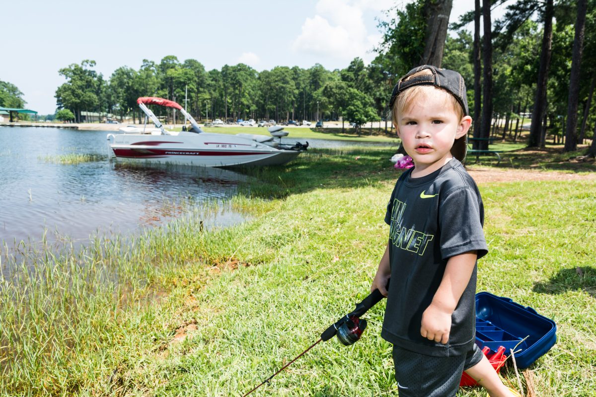 Boy standing with fishing rod with boat in the background