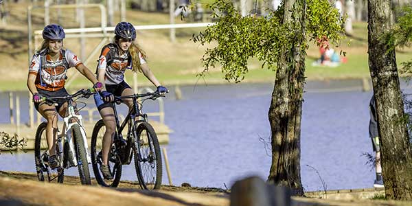 Two women riding mountain bikes near lake on sunny day