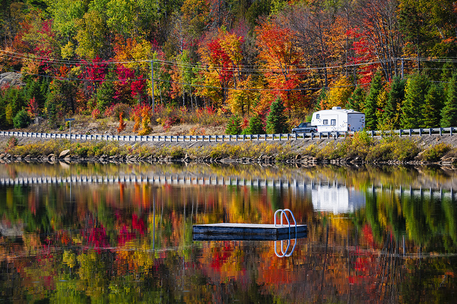 Camper driving though fall forest with colorful autumn leaves reflecting in lake. Highway 60 at Lake of Two Rivers, Algonquin Park, Ontario, Canada.