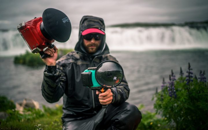 Flylords Photographer holding camera in front of waterfall.