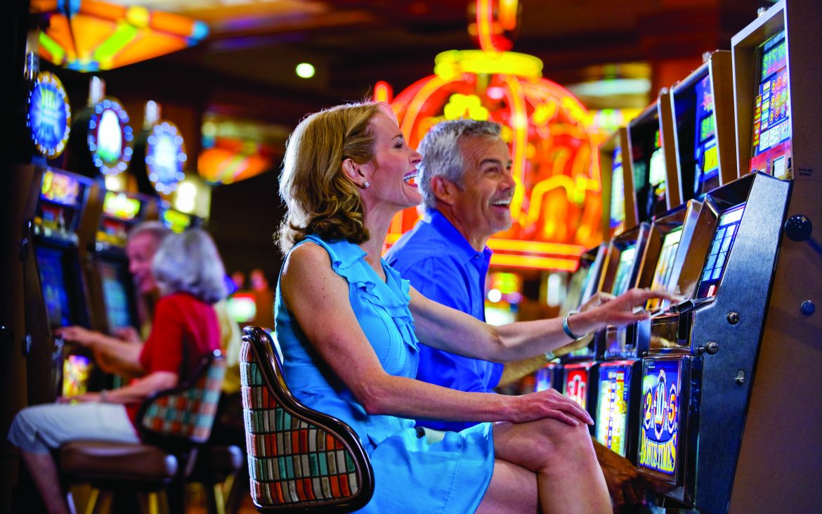 Man and woman sitting at slot machine in busy casino