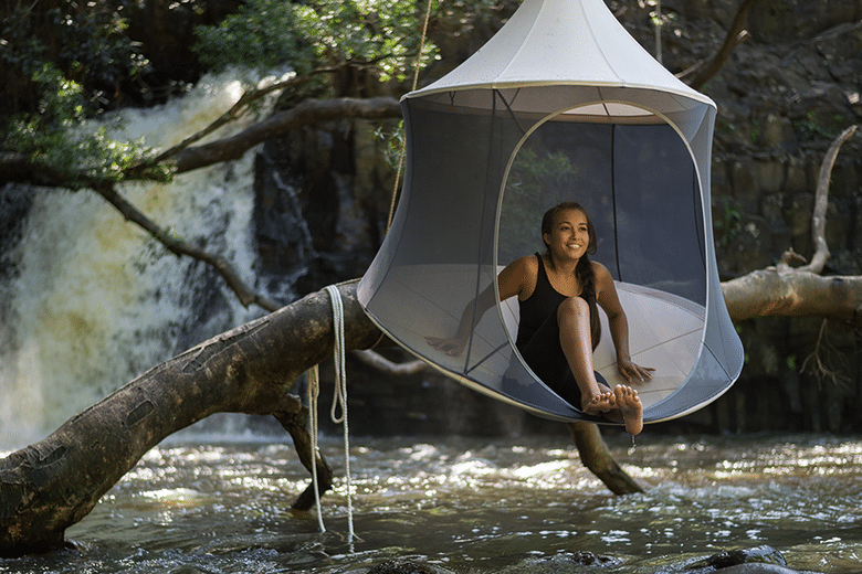 Woman sitting in treepod cabana hanging over a flowing river.