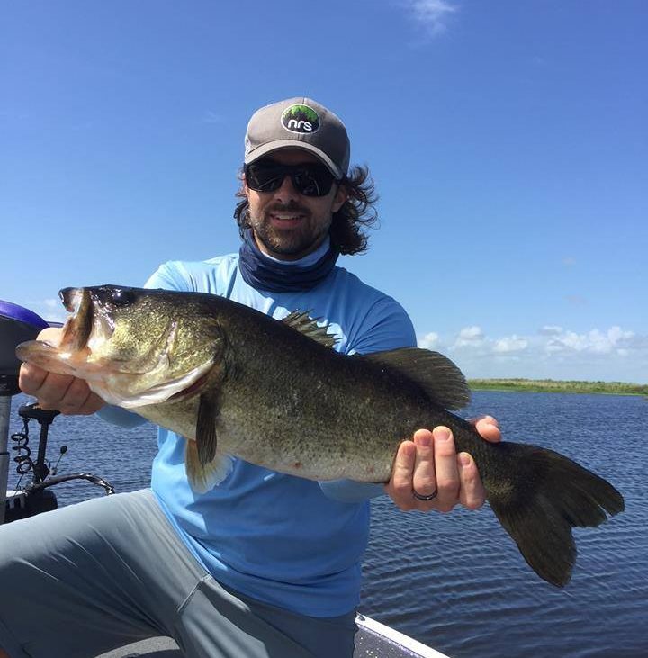 Man wearing baseball hat posing with large bass fish on boat