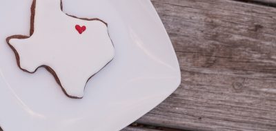 Texas shaped sugar cookie with white icing and a red heart on a rustic wood table.