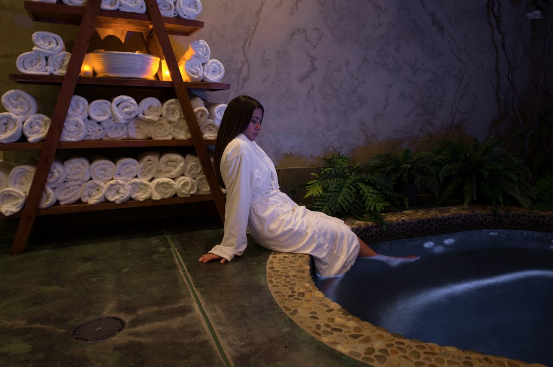 Young woman sitting on edge of jacuzzi in a bathrobe with her feet in the water.
