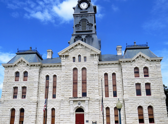 Hood County Courthouse in Granbury, Texas. Architect W.C. Dodson designed the French Second Empire limestone building with ornamental sheet metal tower and cornice. The clock tower is 3 stories. This photo is a revision; I cropped on both sides and all signs, including the historical marker in the foreground.