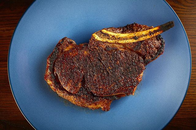 A steak on the bone on a blue plate.