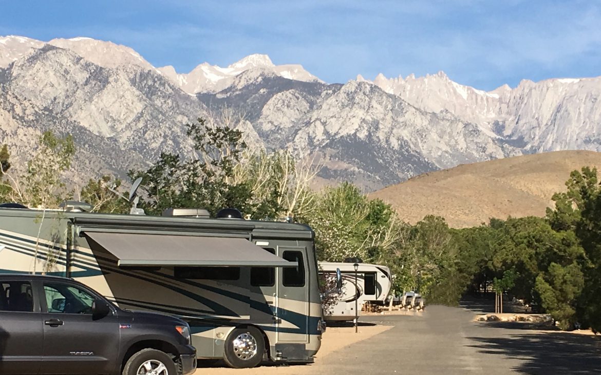 Large truck and RV parked along paved road with mountains in background