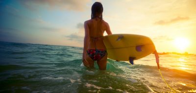 Young lady surfer walking into the sea with board