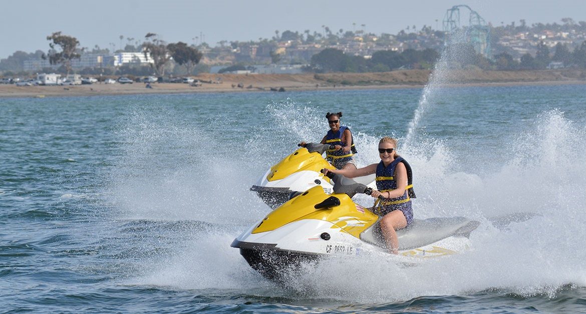 Couple riding yellow and white jet skis on bay