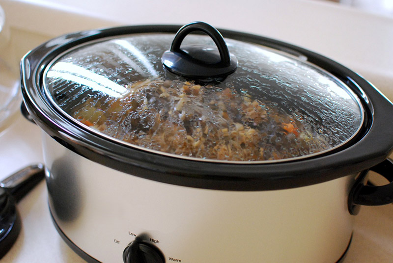 A crockpot with a clear lid simmers with a succulent dinner.