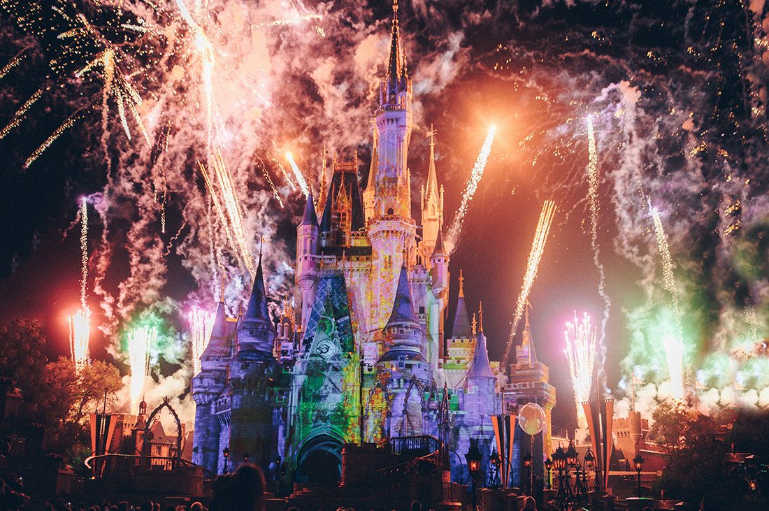 Colorful lit Disney castle at night with fireworks exploding