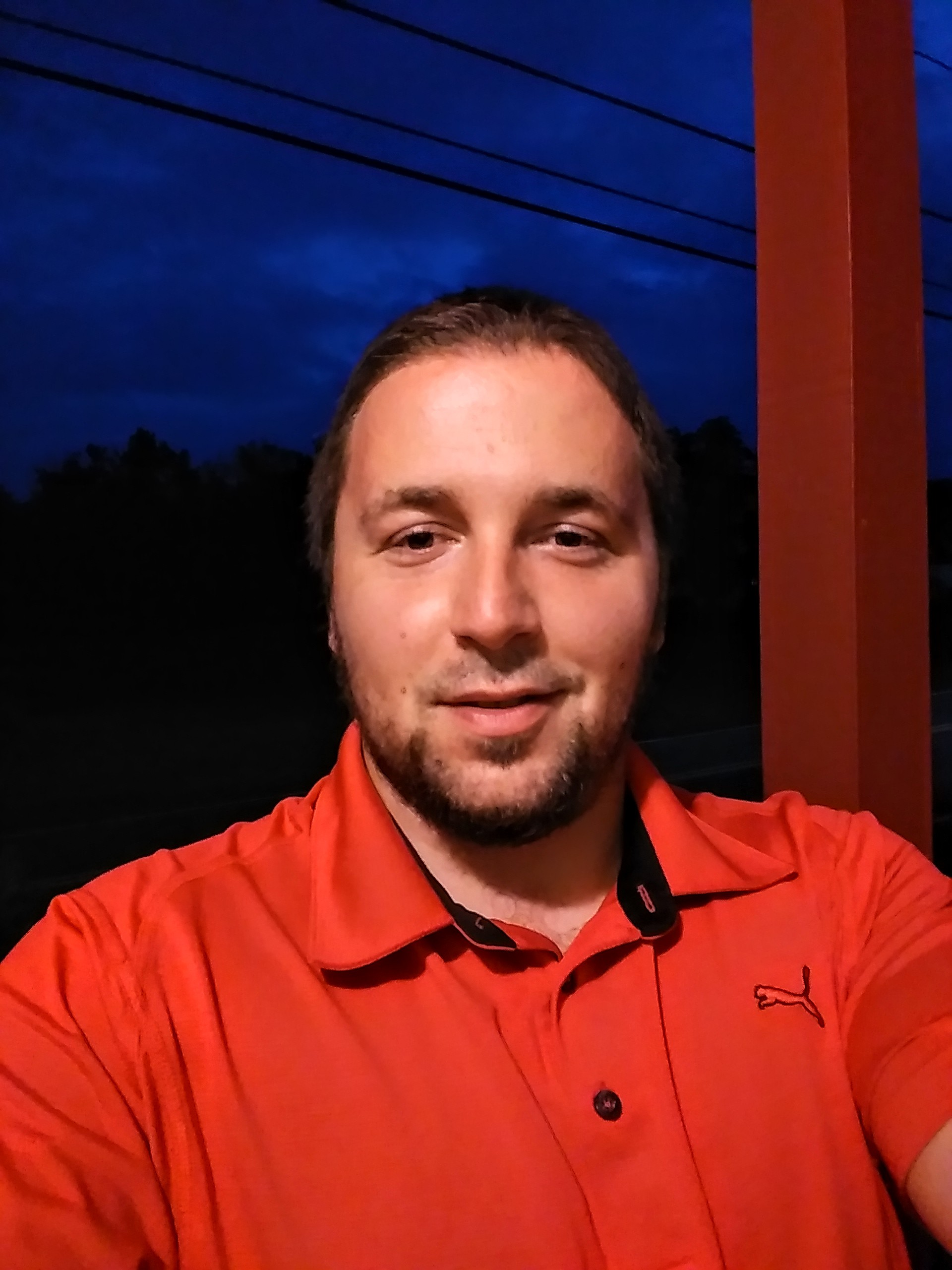 Man with beard and red shirt smiles at camera.