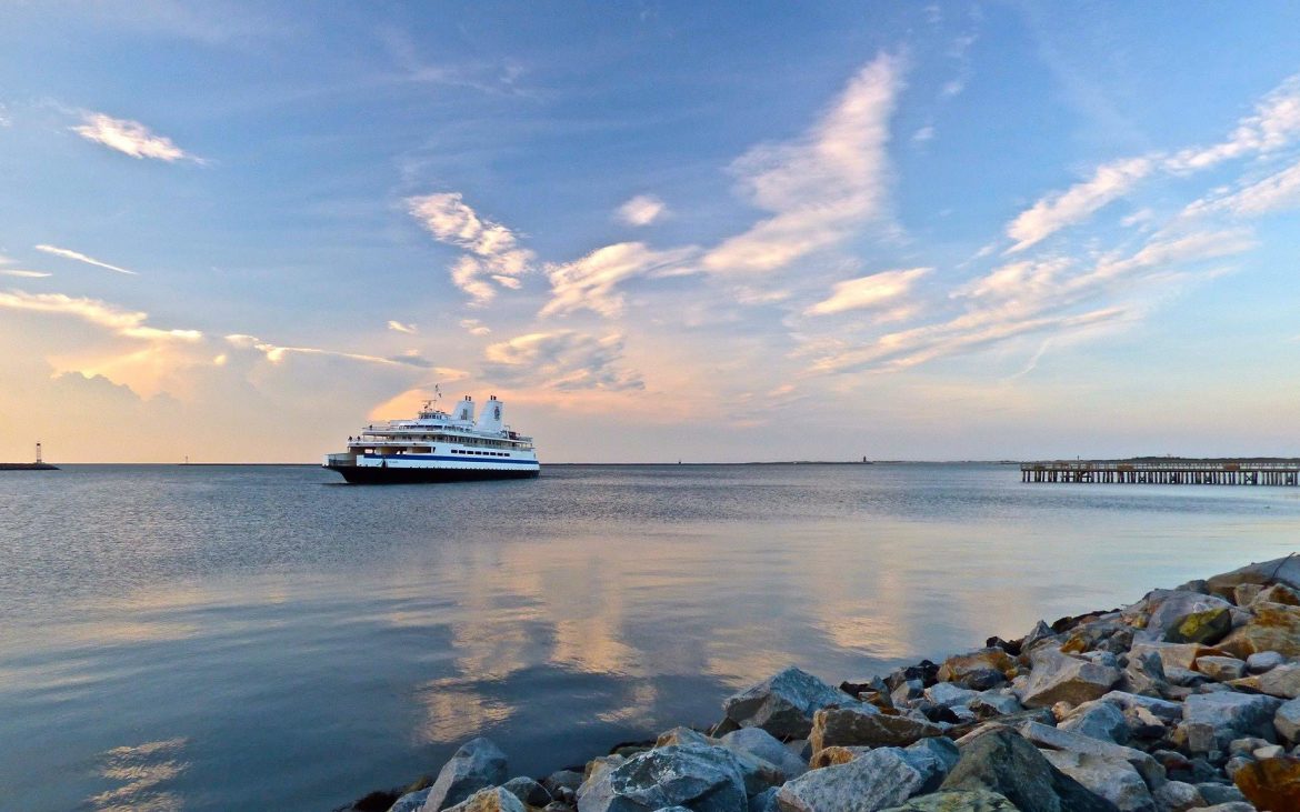 Large cruise ship on ocean waters near pier, with clouds in blue sky