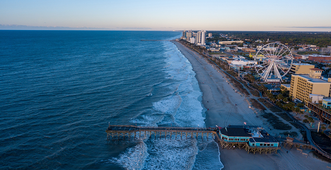 An aerial shot of a beach with pier jutting into ocean and buildings and attractions inland from the sand at Myrtle Beach.