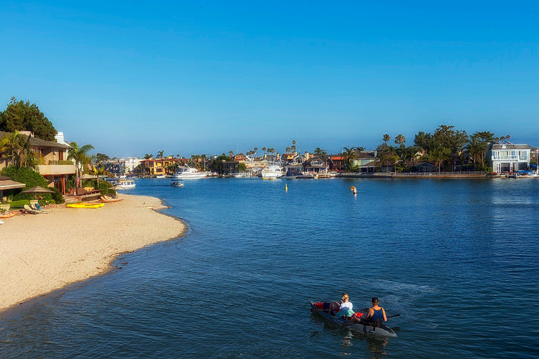 A couple paddle a double kayak through a channel lined with condos in Newport Beach.