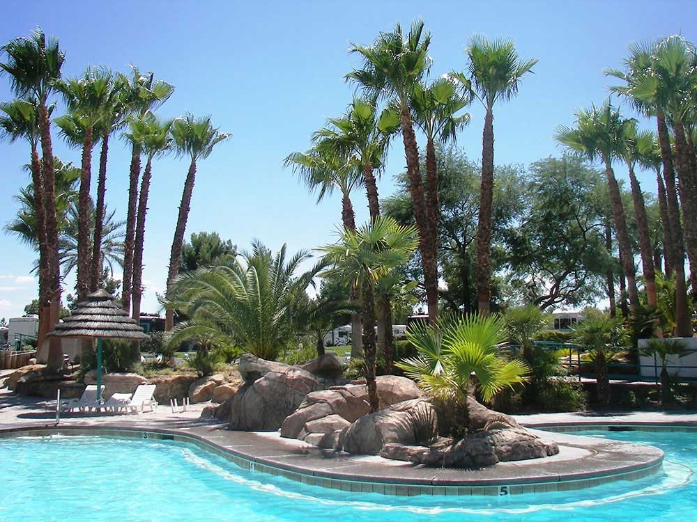 Palm trees and boulders form a tropical landscaping around the aqua-blue waters of the Oasis Las Vegas RV resort pool.