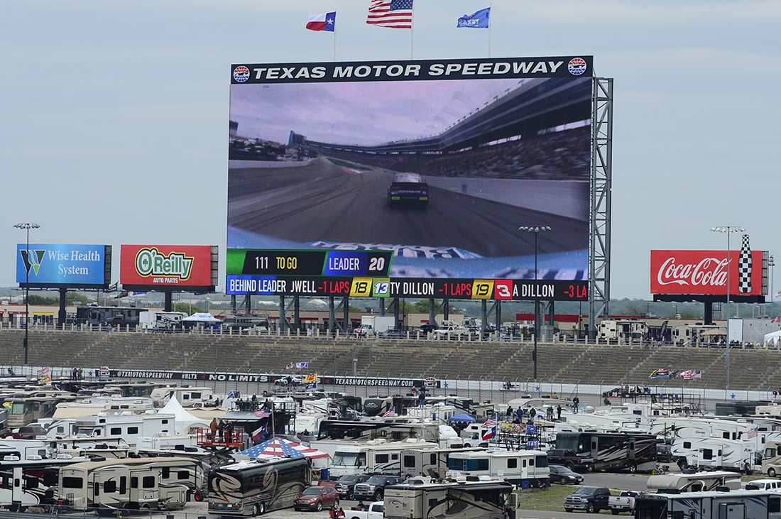 Large screen above Texas Motor Speedway showing NASCAR racing, with RVs in center