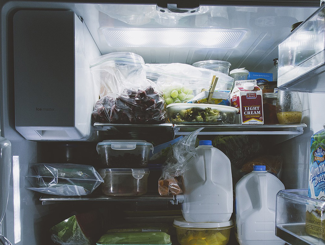 The shelves of a refrigerator are laden with milk, grapes vegetables and other food items.