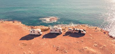 Three Class B RVs parked on a arid bluff overlooking ocean waters.