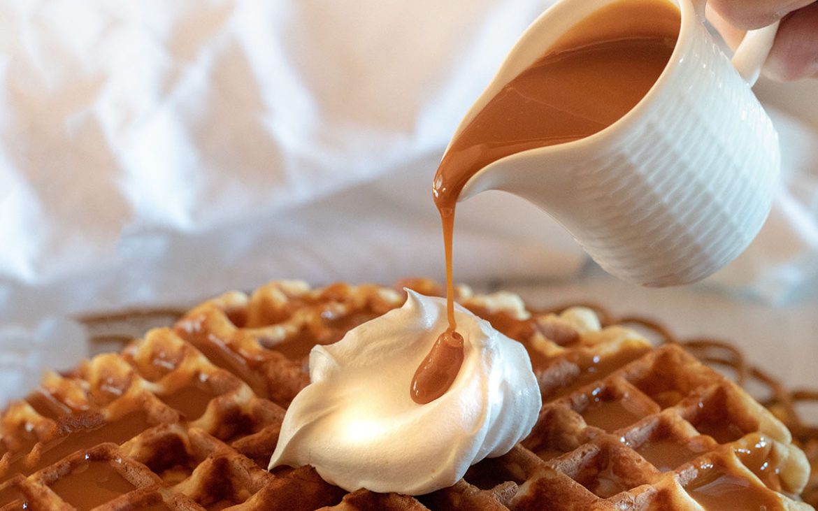 Pouring succulent caramel syrup over a stack of crispy brown waffles.