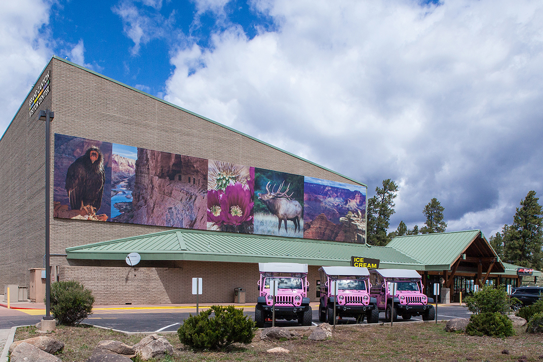 An exterior view of the Grand Canyon Imax theater with pink jeeps in the foreground.