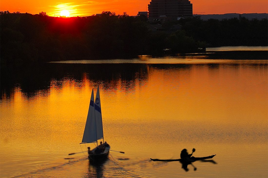A sailboat and kayak share the golden waters of Lady Bird Lake during sunset.