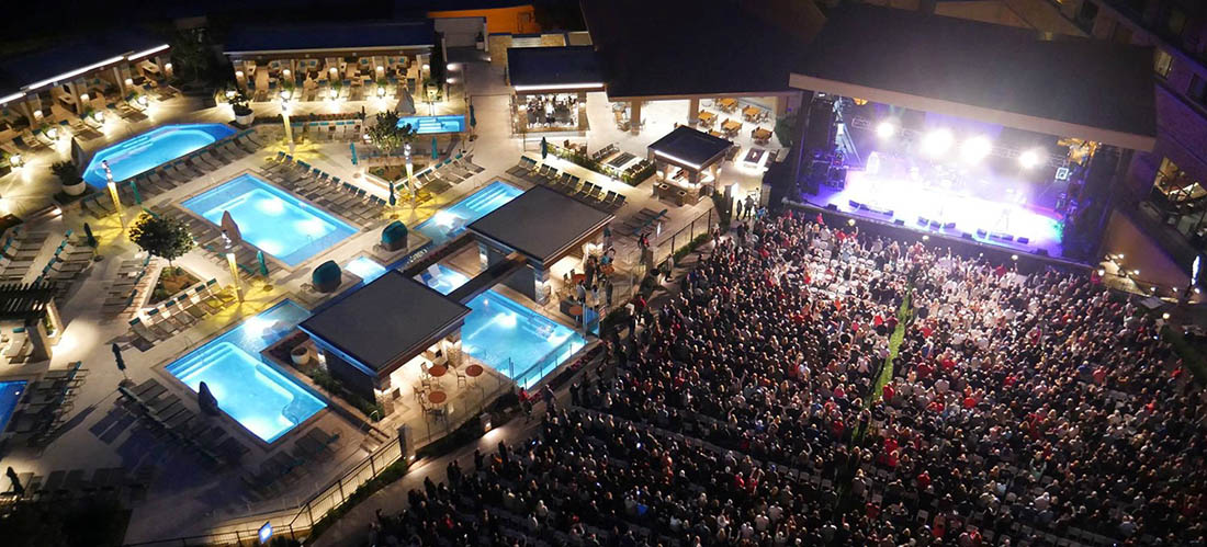 A crowd gathers in front of the stage in an outdoor concert venue.