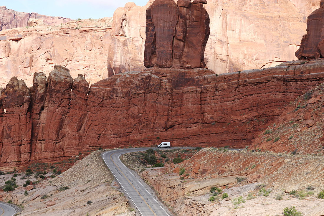 A white camper van descends a winding road with sheer rock walls rising in the background.